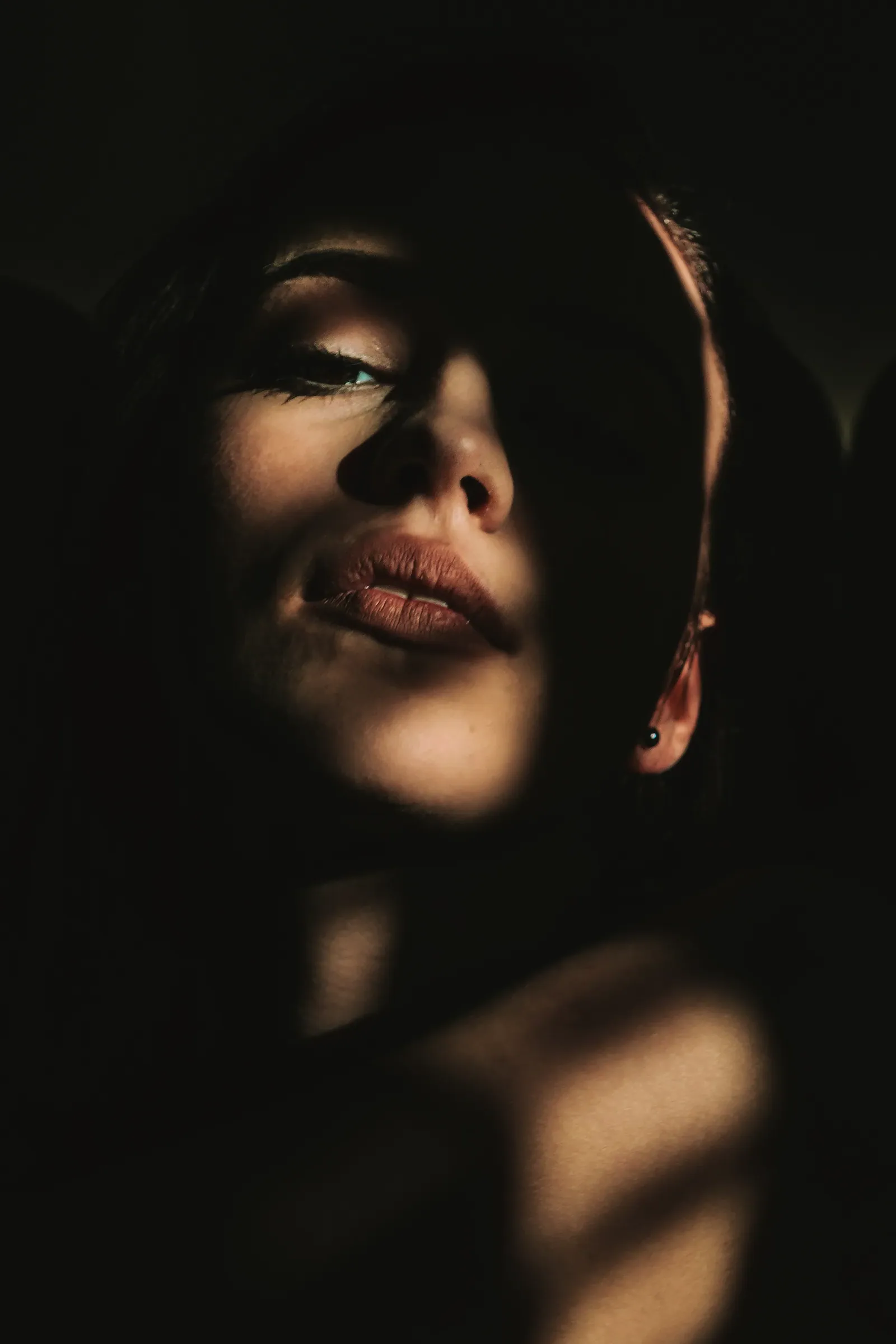 Close portrait of a dark-haired woman in window-blind shadow and warm light