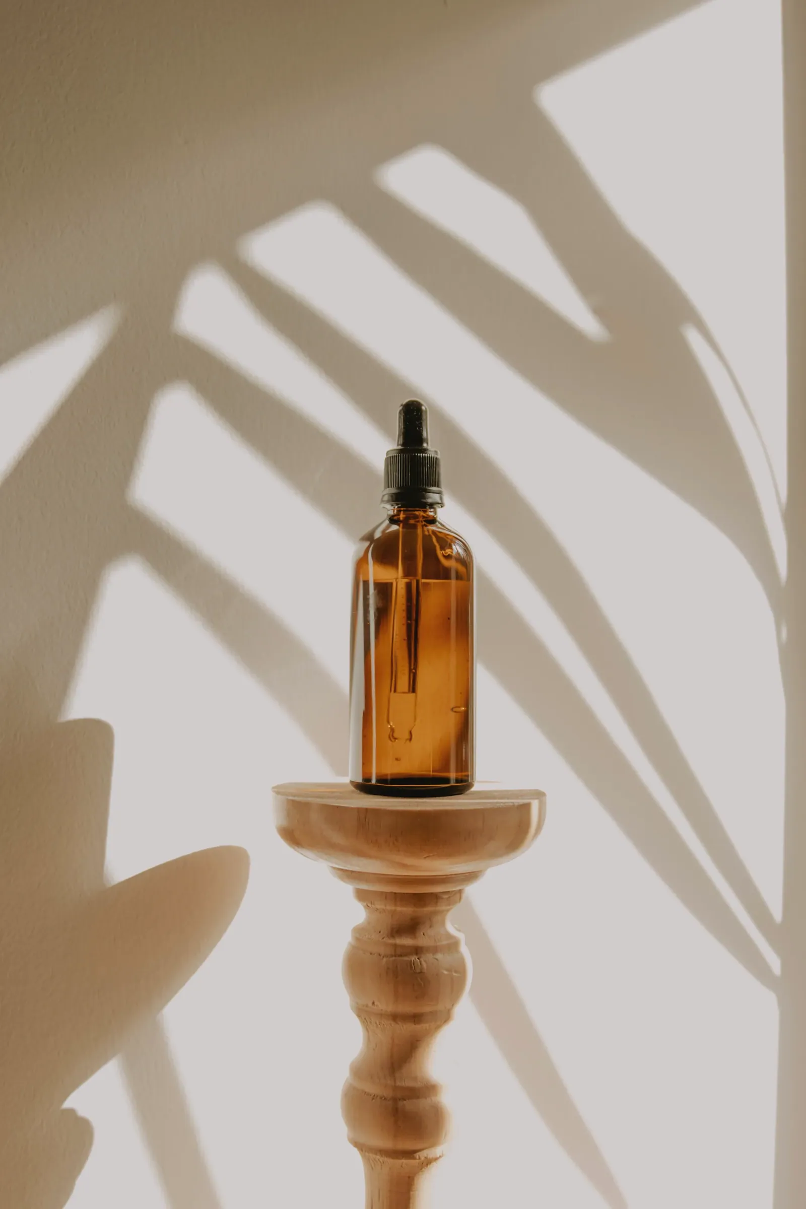 Amber serum bottle on a wooden pedestal with leaf shadows